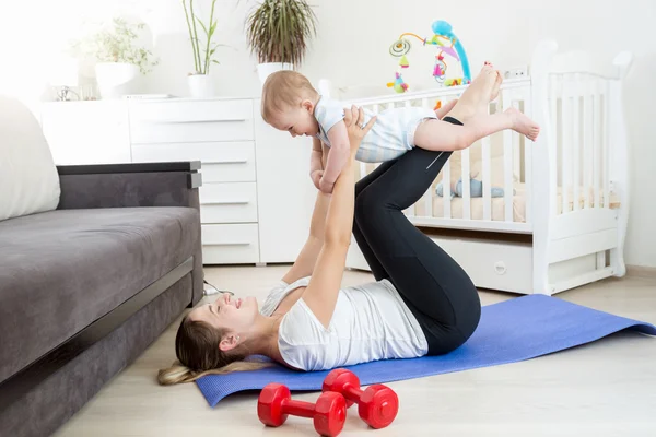 Joven madre y su bebé haciendo yoga en el suelo en la sala de estar — Foto de Stock