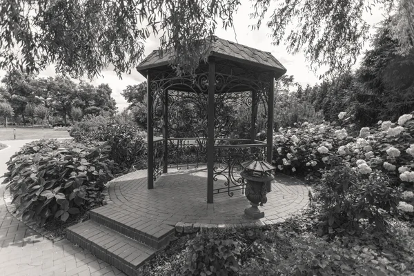 Black and white image of old metal alcove under tree at park — Stock Photo, Image