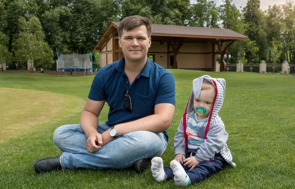 Pohledný mladý otec sedí s jeho 9 měsíců starý syn na trávě — Stock fotografie