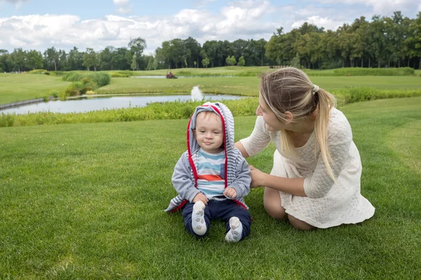 Gelukkig moeder met haar 9 maanden oude babyjongen ontspannen op gras op — Stockfoto