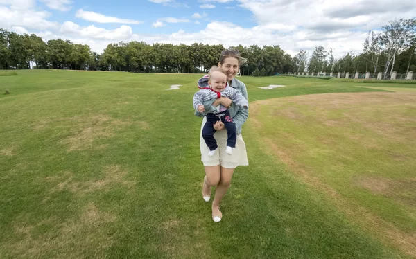 Vrolijke moeder houdt haar babyjongen en draait op gras op gelijke voet — Stockfoto