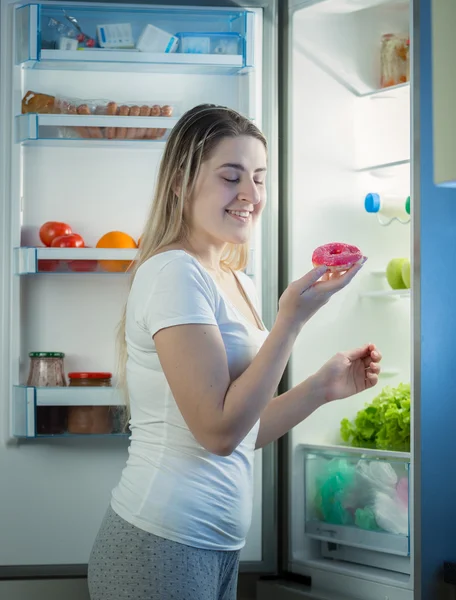 Schöne Frau holt Krapfen am späten Abend aus dem Kühlschrank — Stockfoto