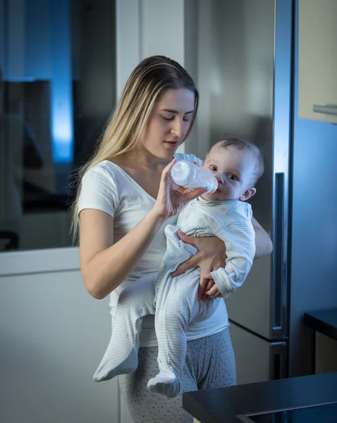 Joven madre dando bebé hijo leche de biberón en la cocina en midn — Foto de Stock