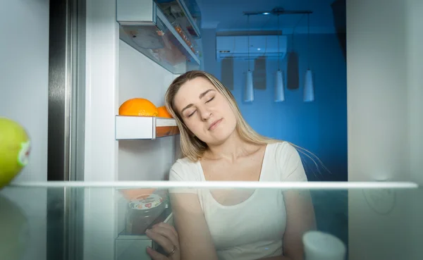 Уставшая женщина в пижаме заглядывает в холодильник в конце дня — стоковое фото