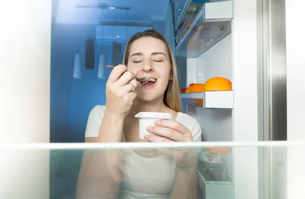 Uitzicht vanaf de binnenkant van de koelkast op vrouw yoghurt eten bij nacht — Stockfoto