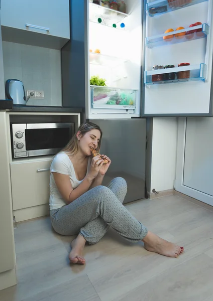 Wanita tanpa tidur duduk di lantai dapur di samping membuka kulkas — Stok Foto
