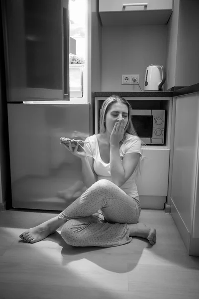 Foto en blanco y negro de la mujer somnolienta sentada al lado del refrigerador abierto — Foto de Stock