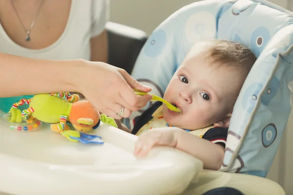 Retrato tonificado de la madre alimentando a su hijo de 9 meses con cuchara —  Fotos de Stock