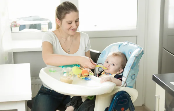 Hermosa madre sonriente alimentando a su bebé en la cocina — Foto de Stock