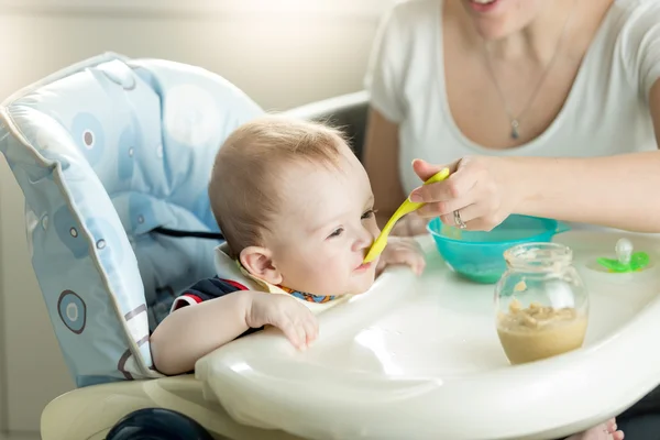 Mother feeding her 9 months old baby son sitting in child chair — Stock Photo, Image