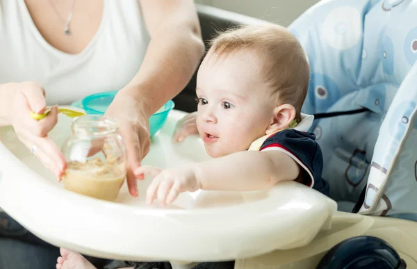 Madre alimentando al bebé con puré de frutas en la cocina —  Fotos de Stock