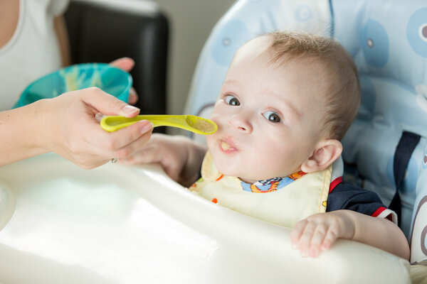 Baby boy in highchair eating apple sauce from spoon