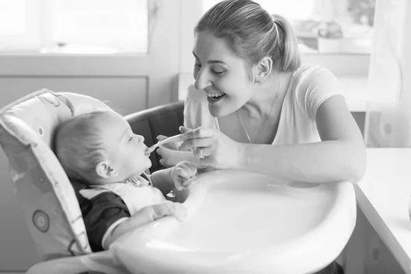 Retrato blanco y negro de la madre sonriente alimentando a su bebé en h —  Fotos de Stock