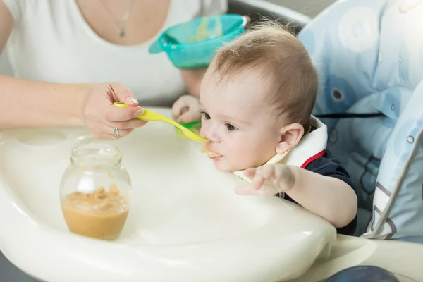 Closeup of 9 months old baby boy eating fruit sauce from glass j — Stock Photo, Image