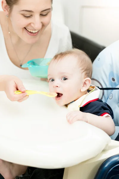 Foto vertical de la madre sonriente dando salsa de manzana a su bebé — Foto de Stock