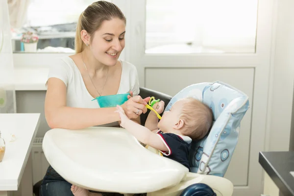 Sonriente joven madre alimentando a su bebé en silla alta — Foto de Stock