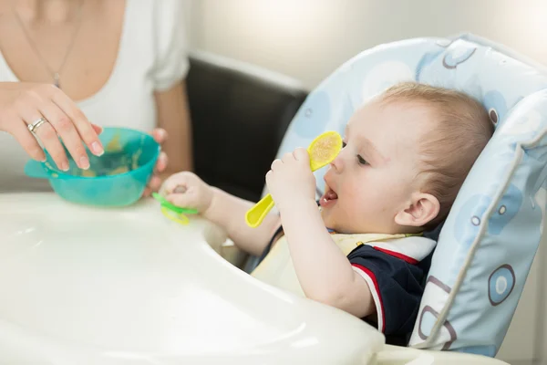 Alegre niño sentado en silla alta y jugando con cuchara —  Fotos de Stock