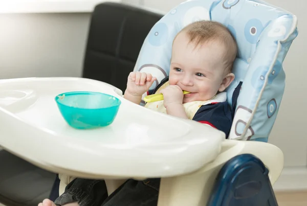 Niño divertido sentado en silla alta y jugando con cuchara y d —  Fotos de Stock