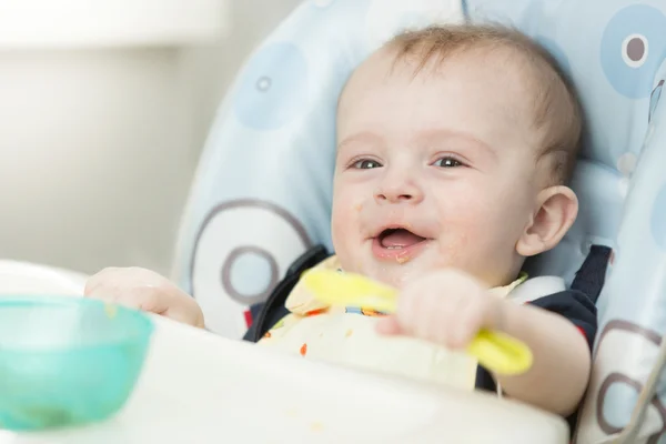 Neşeli gülümseyen bebek çocuk sandalyesi kaşık ile oynarken — Stok fotoğraf