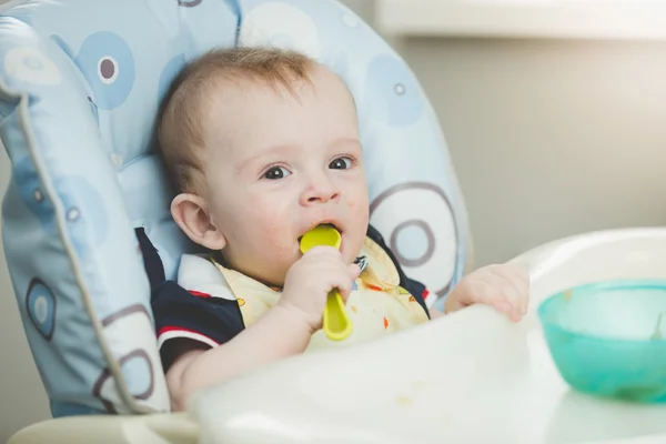 Adorable bebé comiendo de cuchara en trona en la cocina —  Fotos de Stock