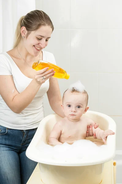 Улыбающаяся молодая мама моет голову ребенку шампунем — стоковое фото