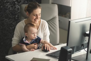 Bilgisayarda çalışan küçük bebek oğlu ile gülümseyen kadın