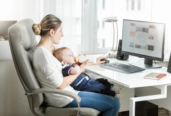Gyönyörű anya otthon dolgozik a Hivatal, és ide-oda a baba etetése — Stock Fotó