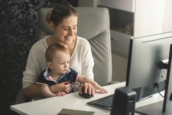 Усміхнена жінка працює за комп'ютером зі своїм маленьким сином — стокове фото