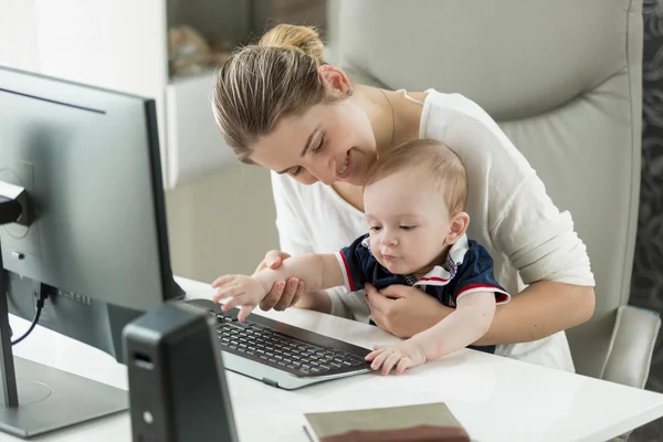 Smiling woman working at home and holding her baby son on lap — Stock Photo, Image