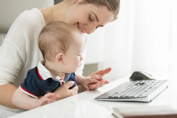 Lycklig mamma sitter vid dator och hålla hennes baby på varvet — Stockfoto