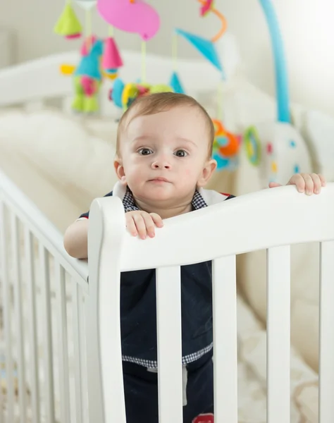 Beautiful 9 months old baby boy standing in crib at bedroom — Stock Photo, Image