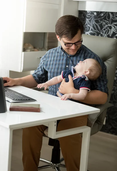 Ung man sitta med sin baby och arbeta hemma — Stockfoto