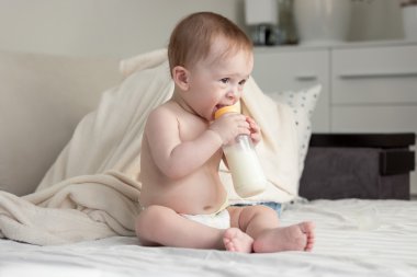 Yatağın üstüne oturan ve içme sütü bott 9 aylık erkek bebek