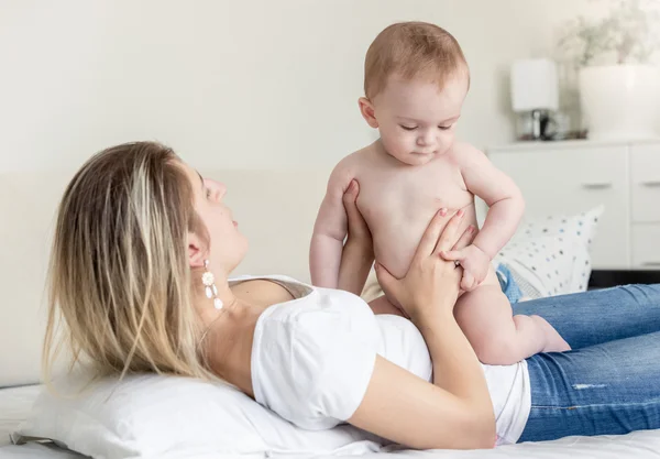 Baby boy in diaper sitting on mother lying on bed — Stock Photo, Image