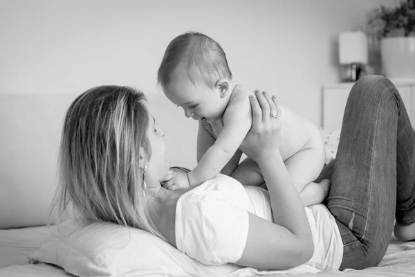 Black and white portrait of happy mother lying on bed and playin