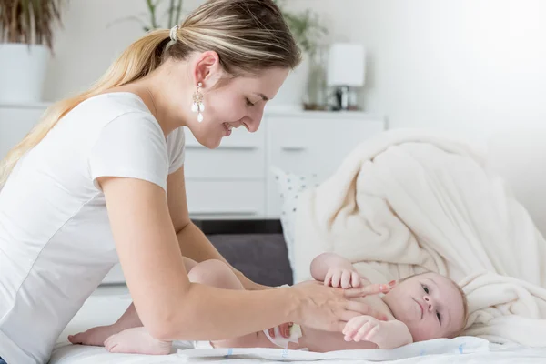 침대에 그녀의 아기의 기저귀를 변경 하는 행복 한 젊은 어머니 — 스톡 사진