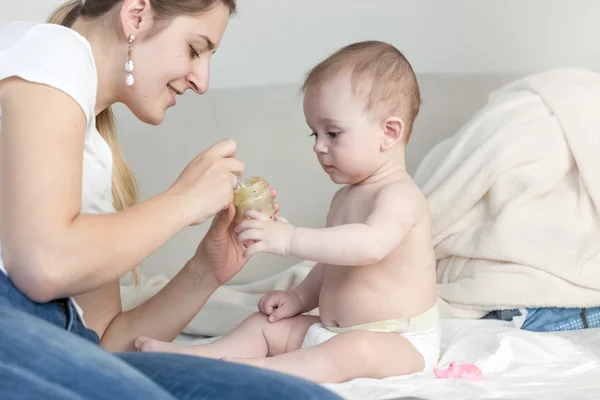 Matka, karmienia jej adorable baby boy na łóżku z sosem owocowym fro — Zdjęcie stockowe