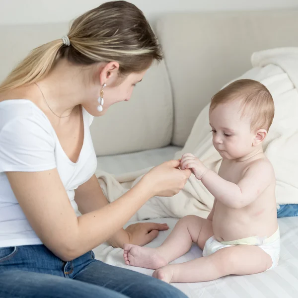 Bela jovem mãe sentada com seu bebê no sofá e dando — Fotografia de Stock