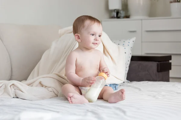 Bebê bonito em fraldas sentado na cama com mamadeira de leite — Fotografia de Stock