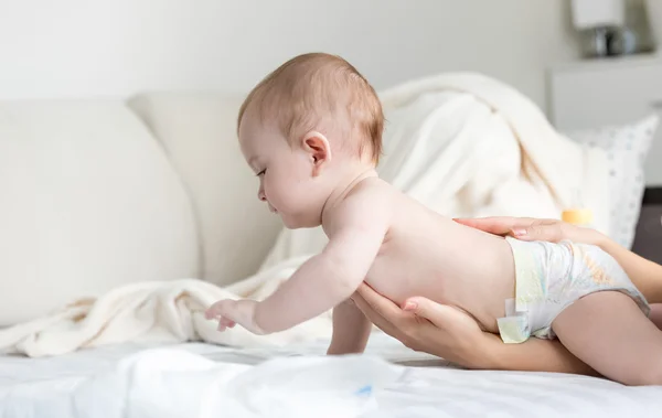 9 months old baby in diapers crawling on bed while mother is hel — Stock Photo, Image