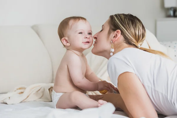 Gyönyörű fiatal anya csókolózás baba fiú arcát ágyon — Stock Fotó