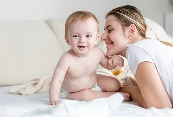 Feliz bebé sonriente sentado con su madre en la cama en el dormitorio — Foto de Stock