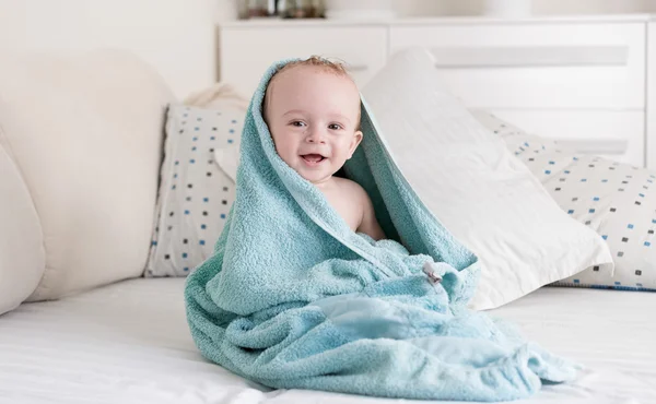 Bebê sorridente coberto de toalha azul depois de tomar banho — Fotografia de Stock