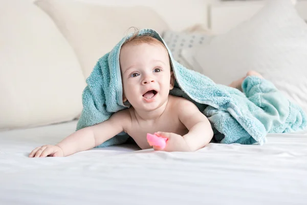 Счастливый улыбчивый малыш под синей игрушкой ползает по кровати с белыми — стоковое фото
