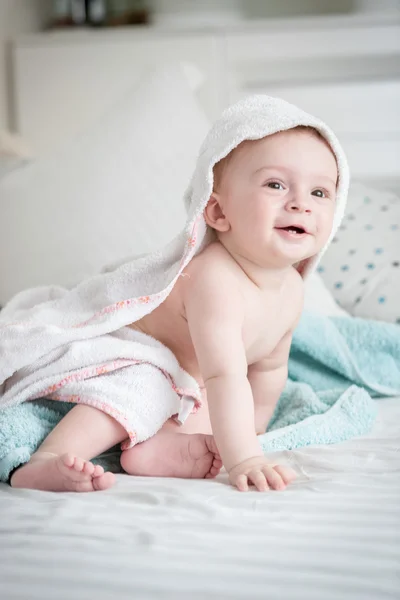 Smiling 9 months old baby boy sitting on bed covered in towel af