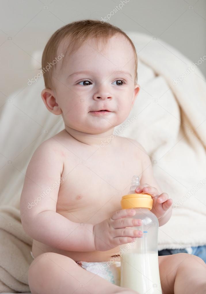 Adorable baby boy in diapers sitting on sofa and holding bottle — Stock Photo © Kryzhov 123421558
