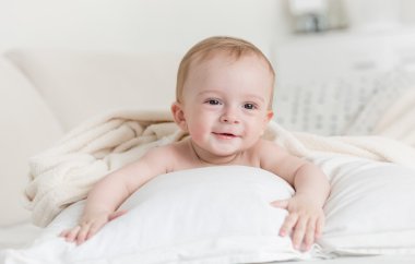 Neşeli büyük yatakta yatarken bebek boy gülümseyerek