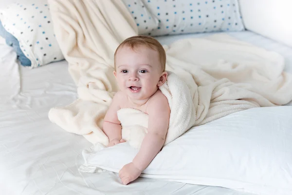 Cheerful baby boy lying on big pillow under white blanket