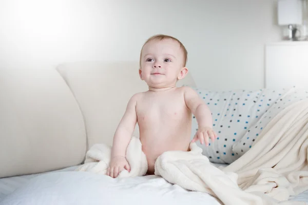 Bébé garçon souriant en couches assis sur le lit avec des draps blancs — Photo