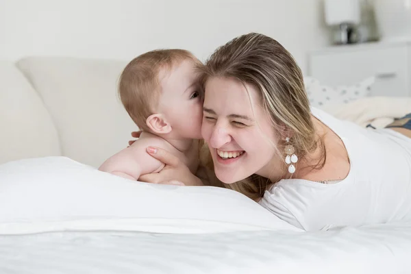 Feliz madre riendo jugando con su bebé en la cama —  Fotos de Stock